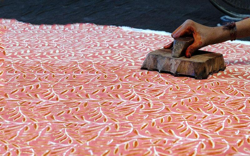 Artisan pressing intricate carved teak block onto fabric